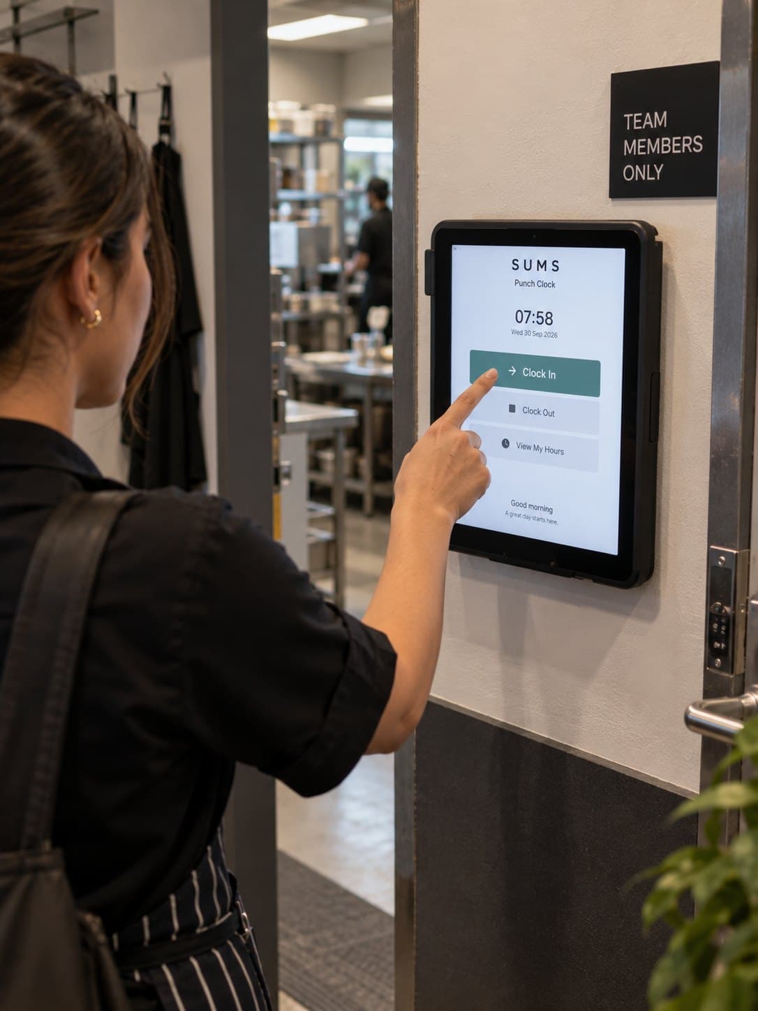 A team member clocking in on a wall-mounted tablet running SUMS Punch Clock at the staff door